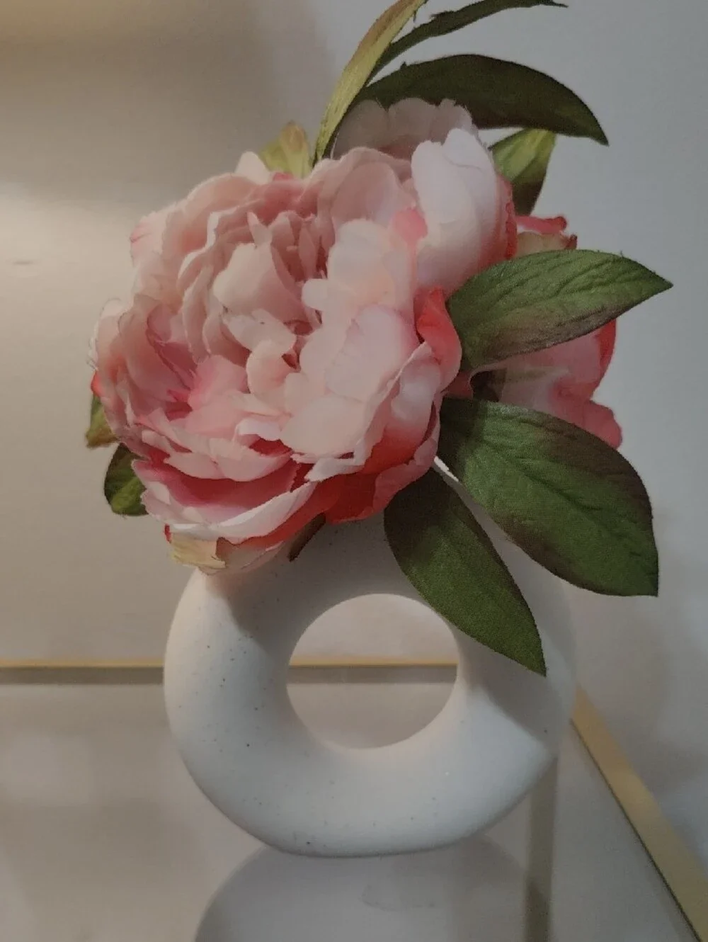 White Donut Ceramic Vase with Beautiful Pink Peony Flowers and Green Leaves.